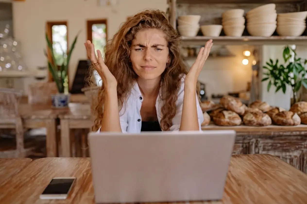 A baker throwing her hands up at a laptop in her bakery